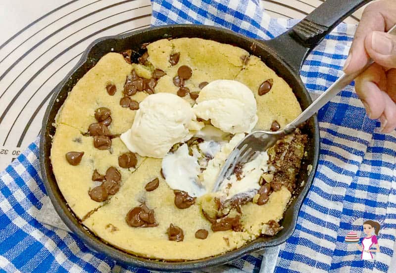 A giant chocolate chip cookie in a skillet, with ice cream on top.