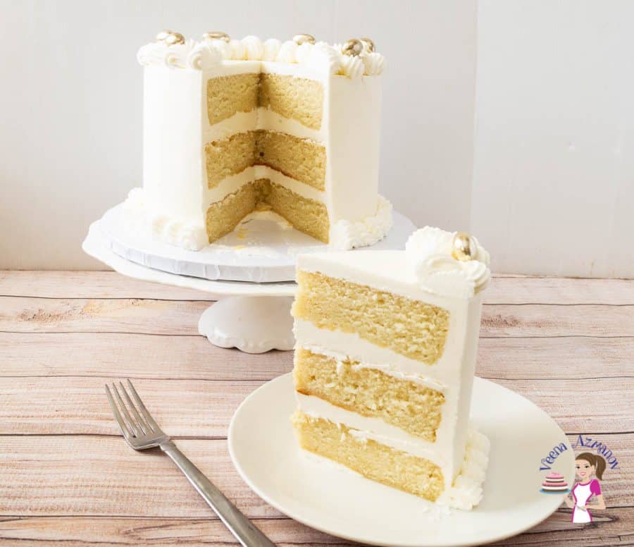 A slice of vanilla layer cake on a plate, with the rest of the cake on a cake stand.