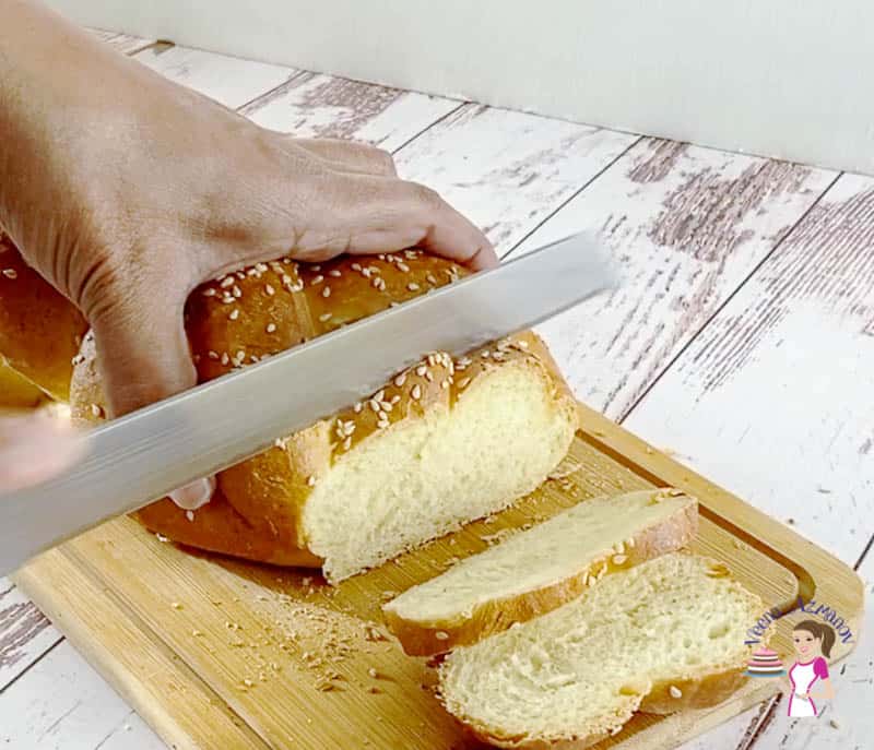 A person slicing challah bread on a wooden board.