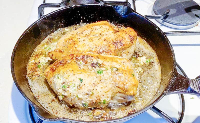 Two cheese-stuffed chicken breasts in a frying pan.