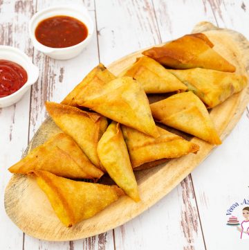 A stack of samosas on a wooden board.