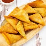 Deep fried samosas on a wooden board.