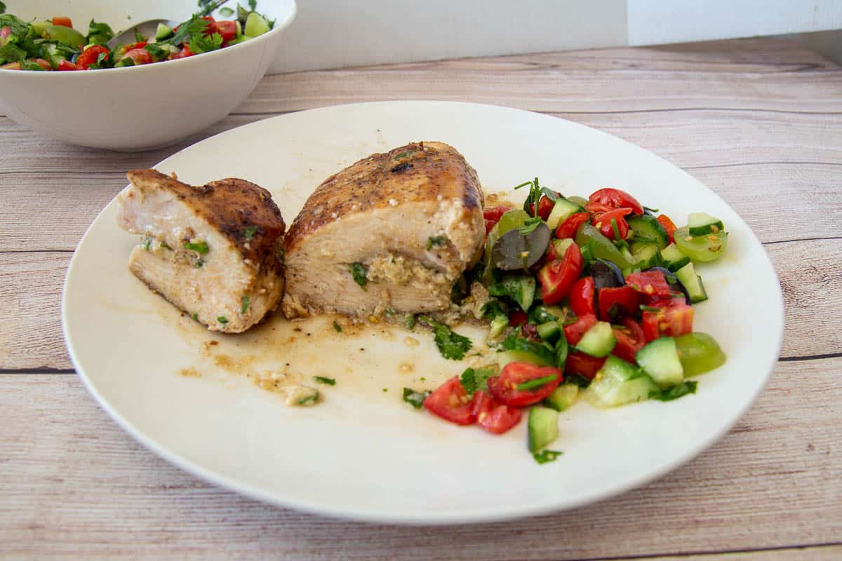 A plate with a cut cheese-stuffed chicken breast and tomatoes and cucumbers salad.