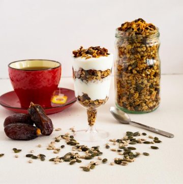 Granola in a jar next to a glass with yogurt parfait.