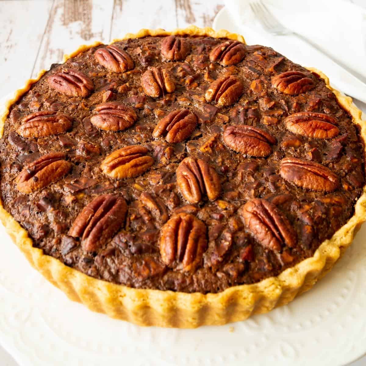 A chocolate pie with pecans on a cake stand.