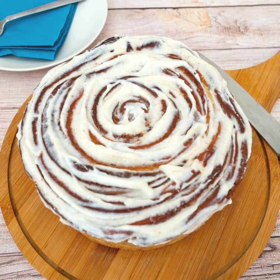 A large cinnamon roll on the wooden board.