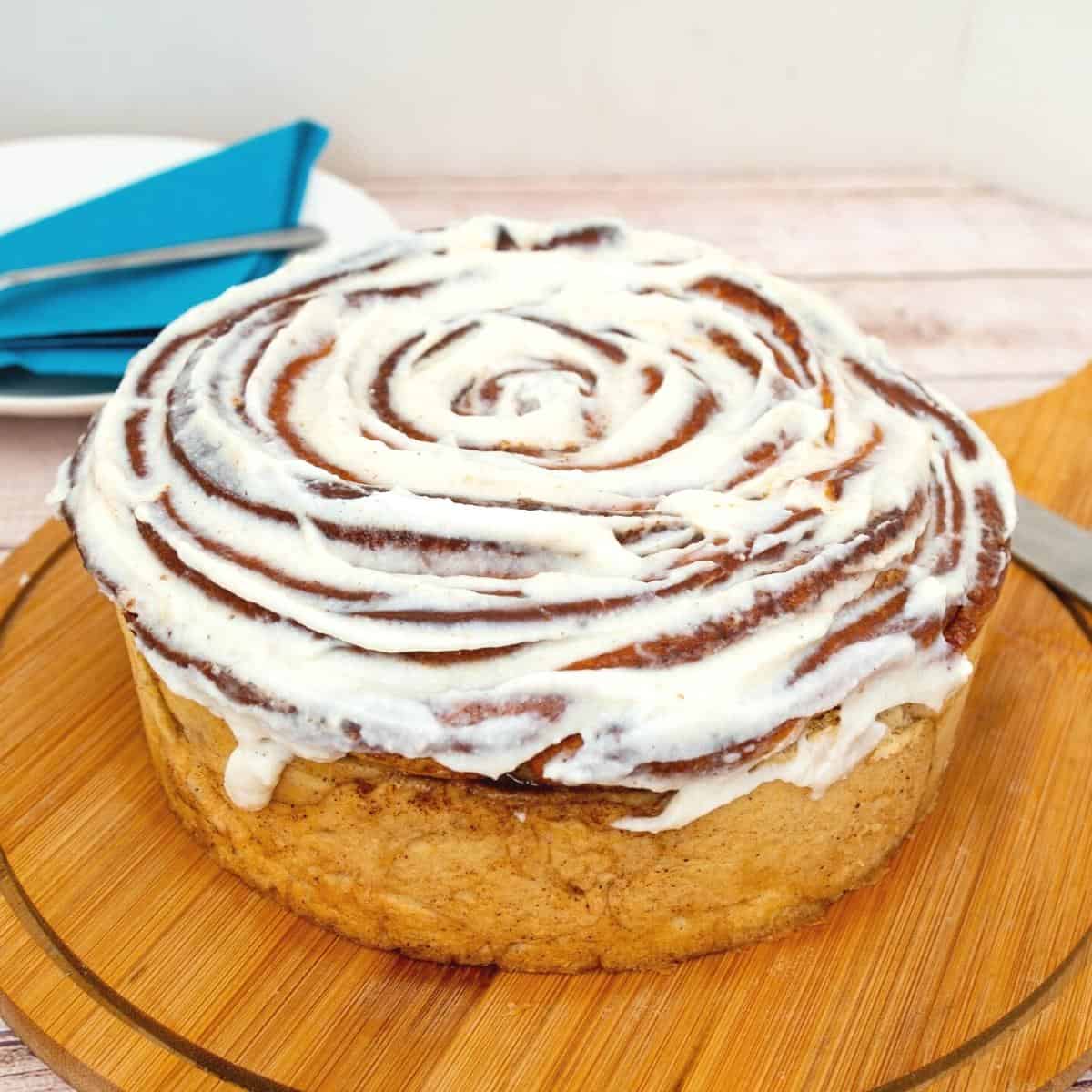 A giant cinnamon roll on the wooden board.