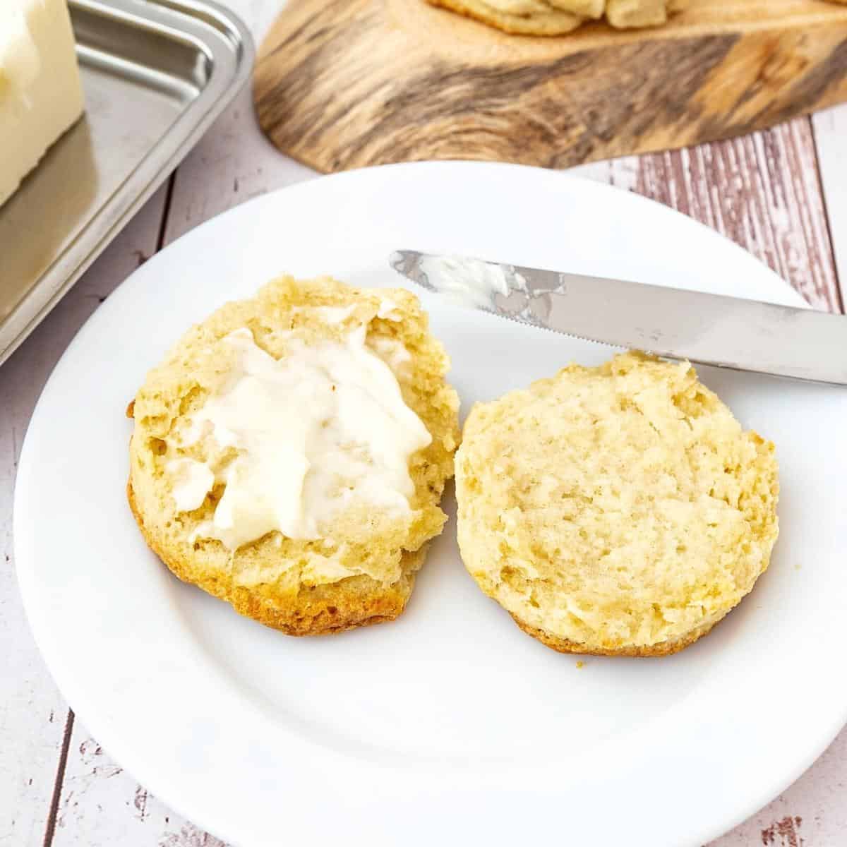 A sliced biscuit with butter on a plate.