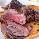 A wooden platter with sliced leg of lamb.