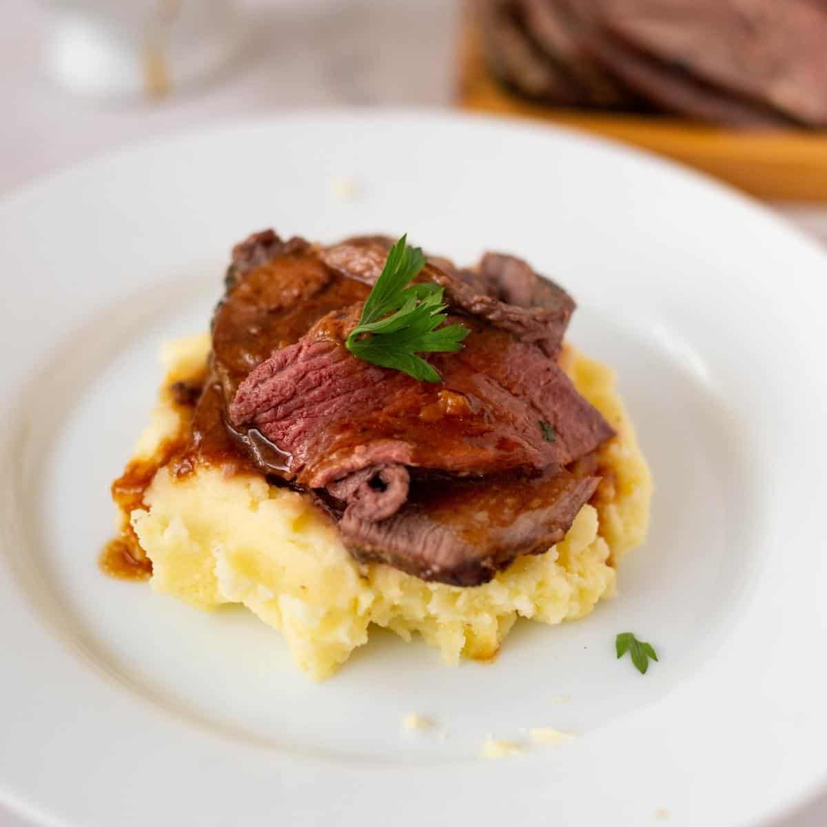 A plate with mashed potato with leg of lamb slices.
