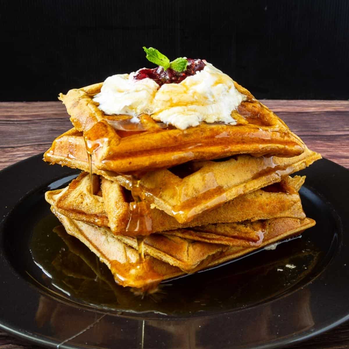 A stack of waffles on a plate with whipped cream.
