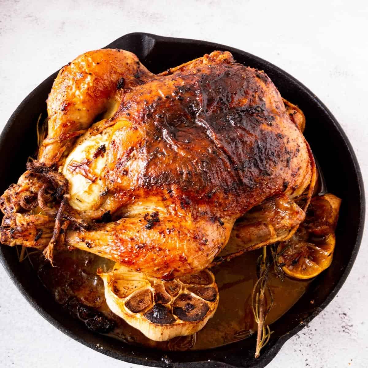 A cast iron skillet with roasting chicken.