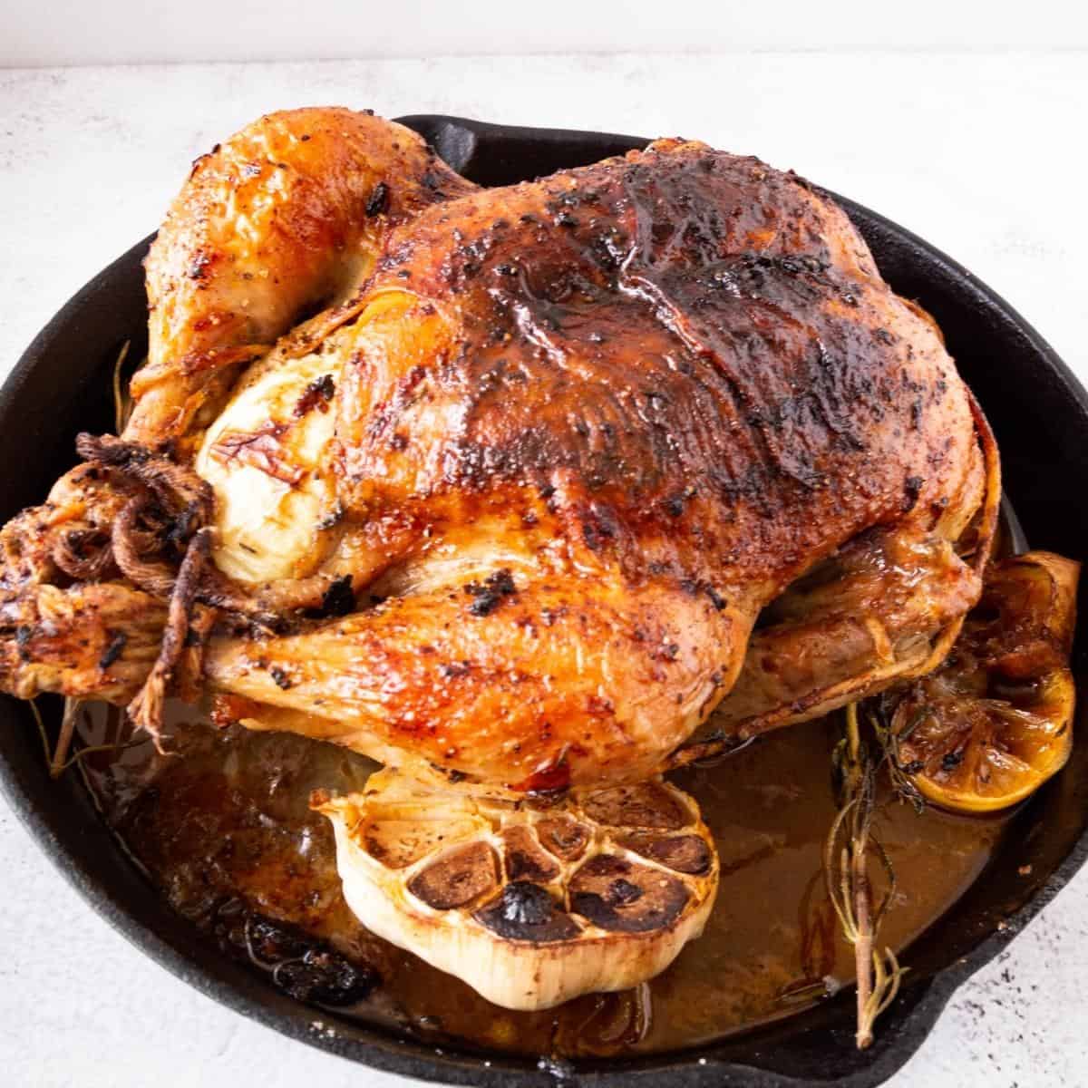 A cast iron skillet with whole roasted chicken.