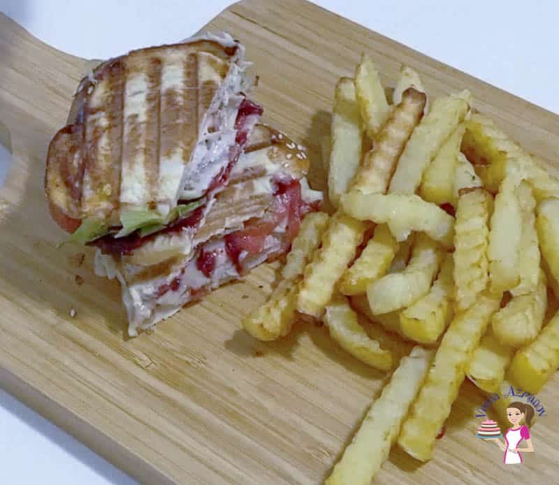 Two half sandwiches on a wooden board with fries