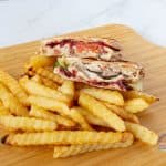 Two half sandwiches on a wooden board with fries