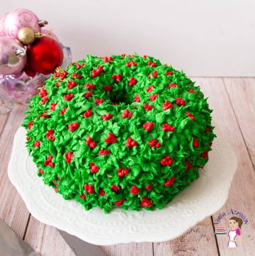 A frosted cake with holly leaves and berries on a cake stand