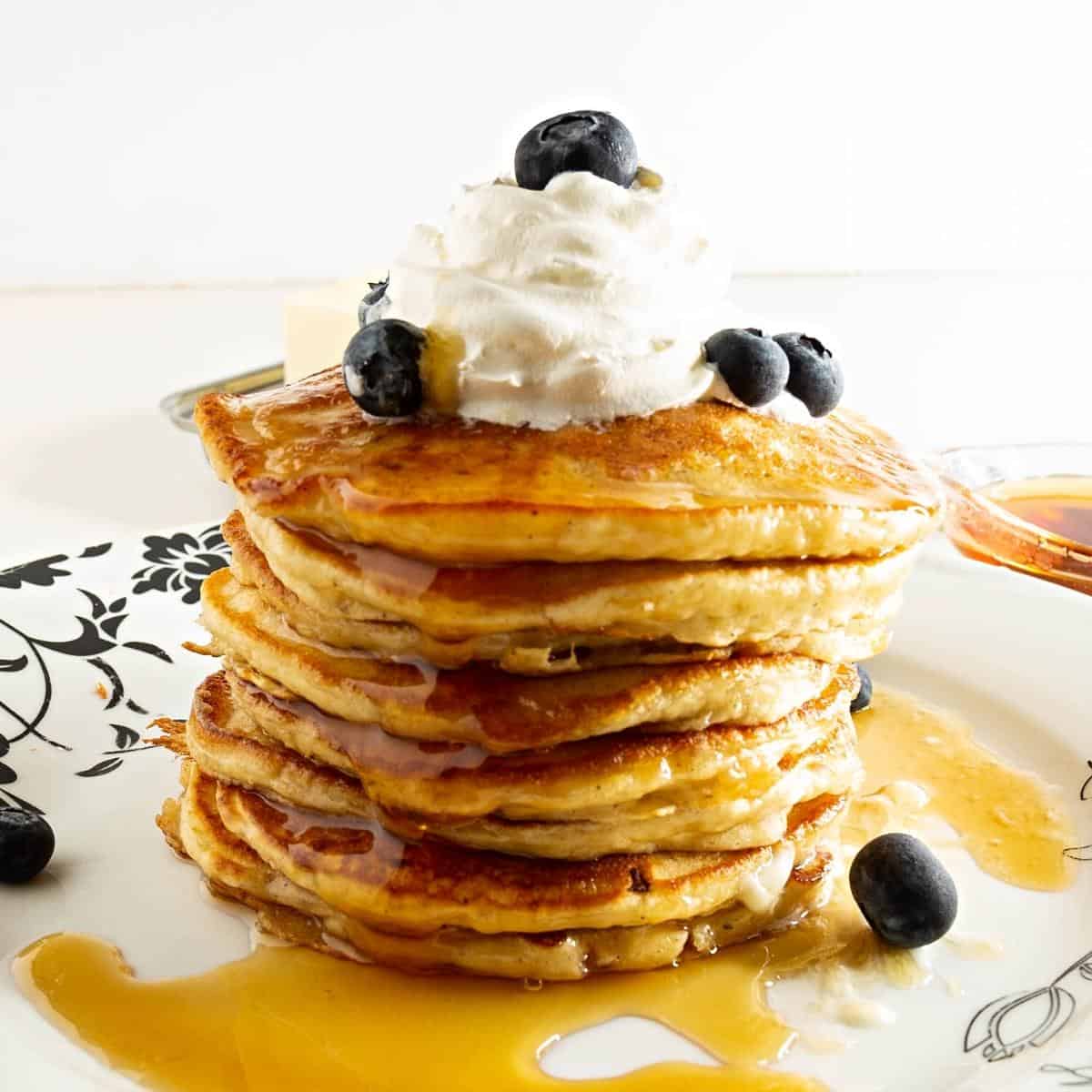 A stack of pancakes with whipped cream and blueberries.