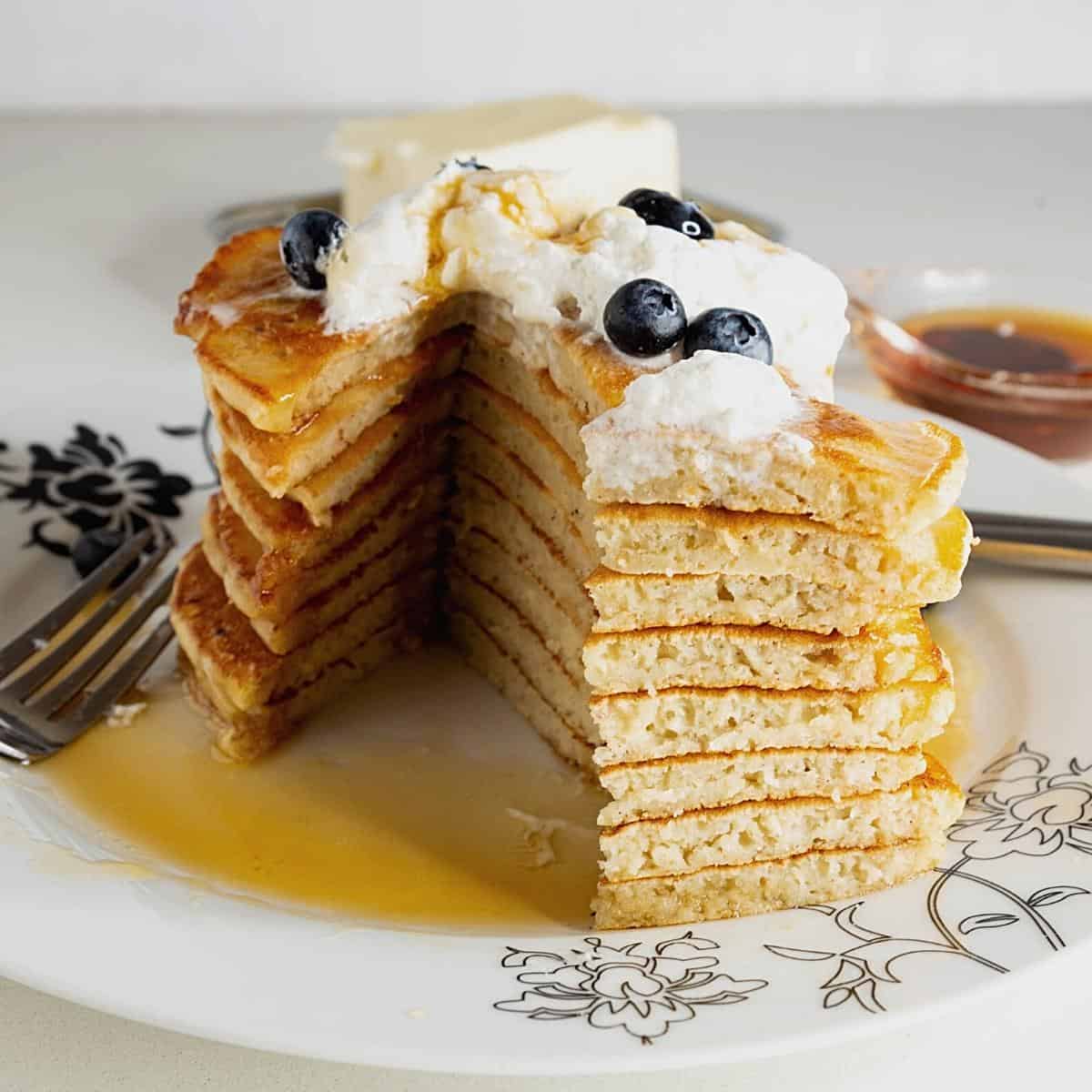 A sliced stack of pancakes with whipped cream and blueberries.