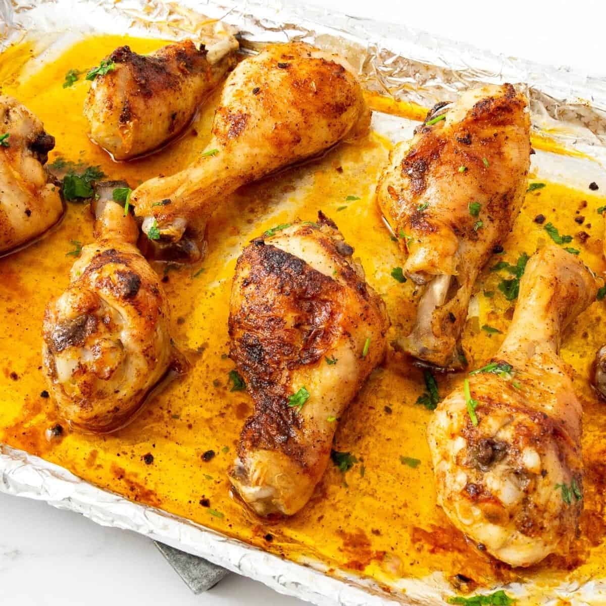A baking tray with chicken drumsticks on a table.