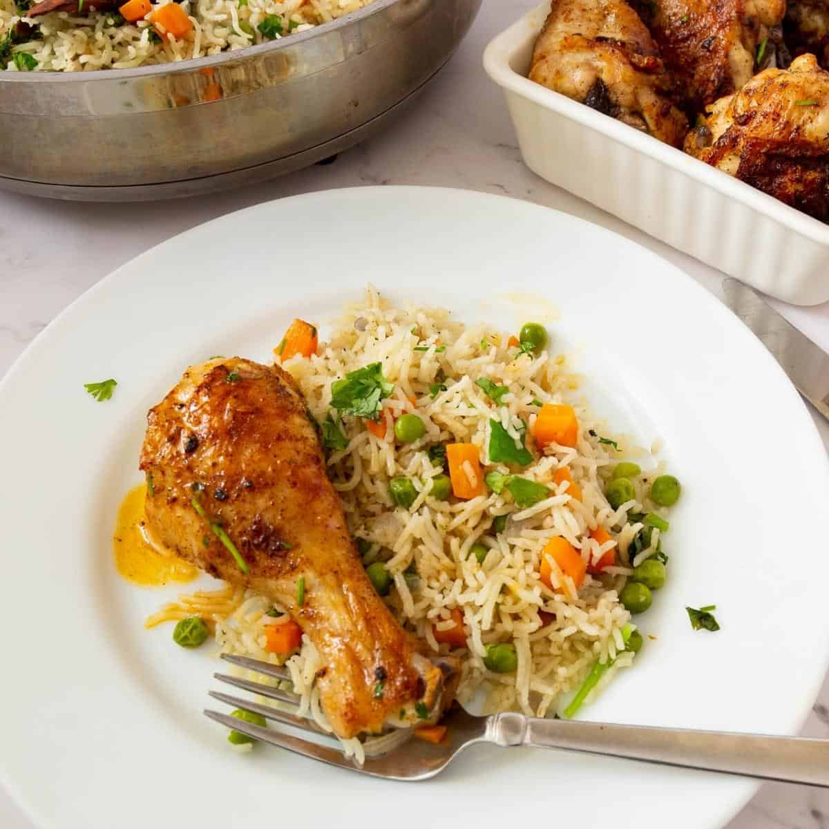 Vegetable rice with baked chicken drumstick on a plate.