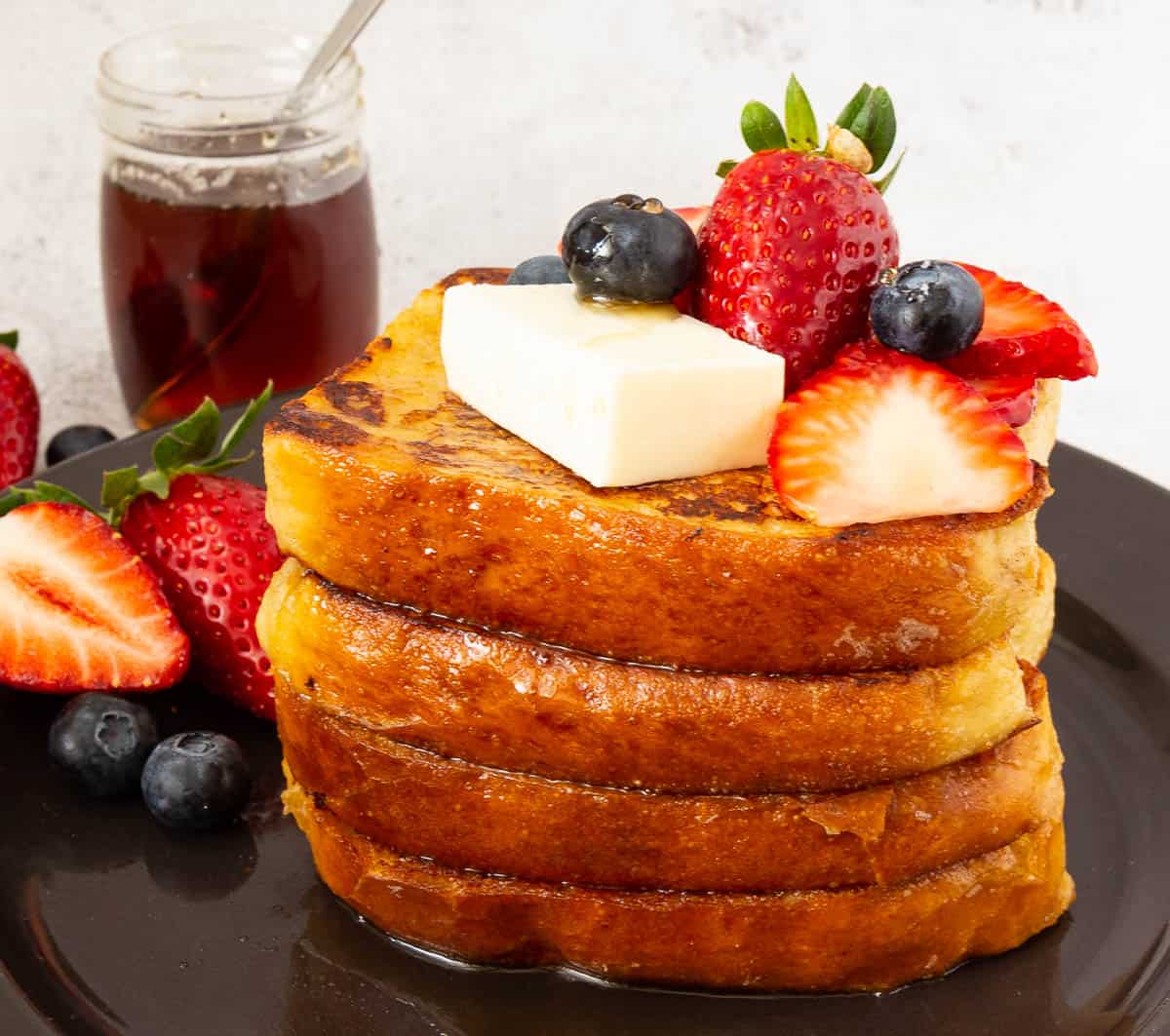 Stack of French toast on a plate with butter and fresh fruits