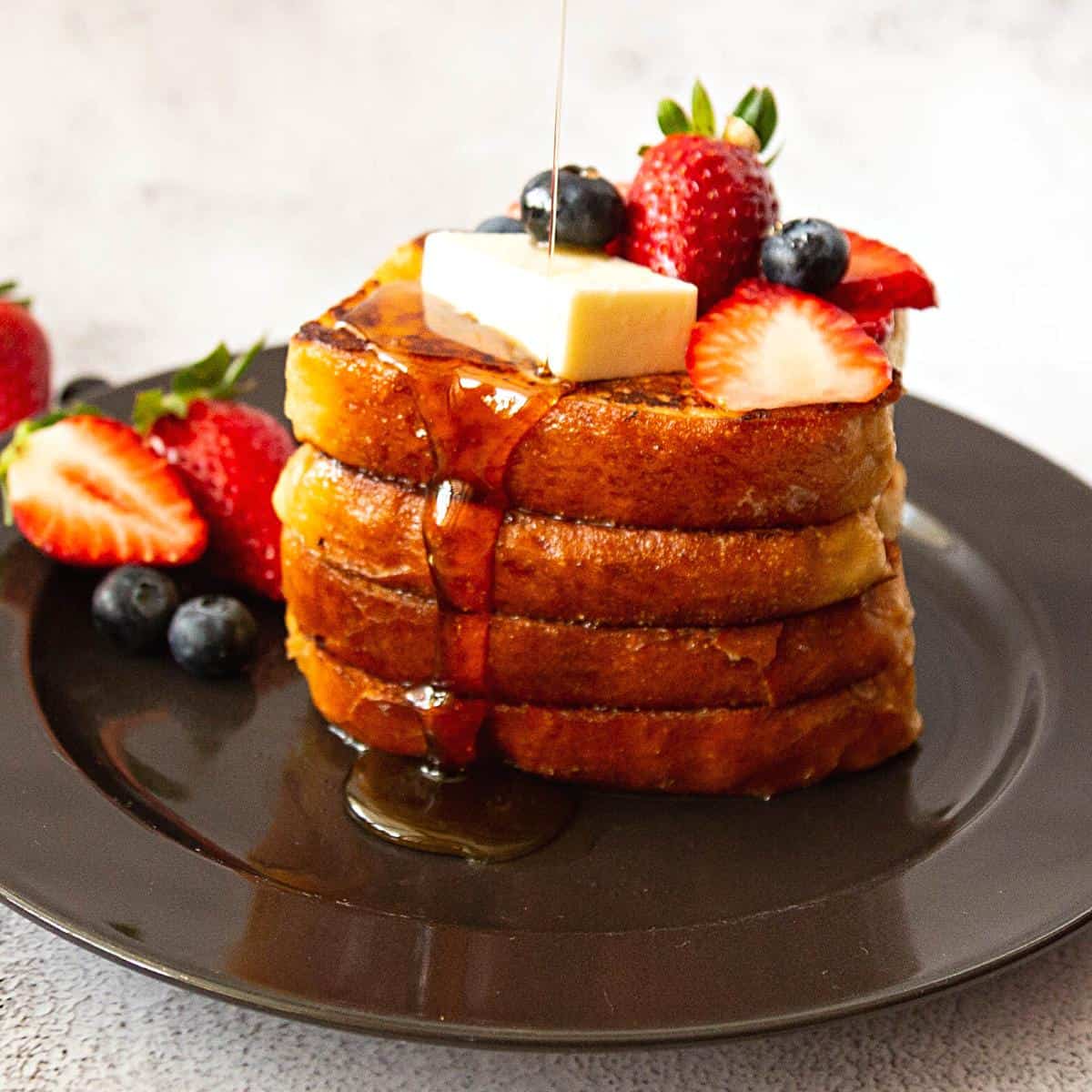 A black plate with French Toast and syrup.