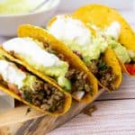 4 filled tacos on a wooden board.