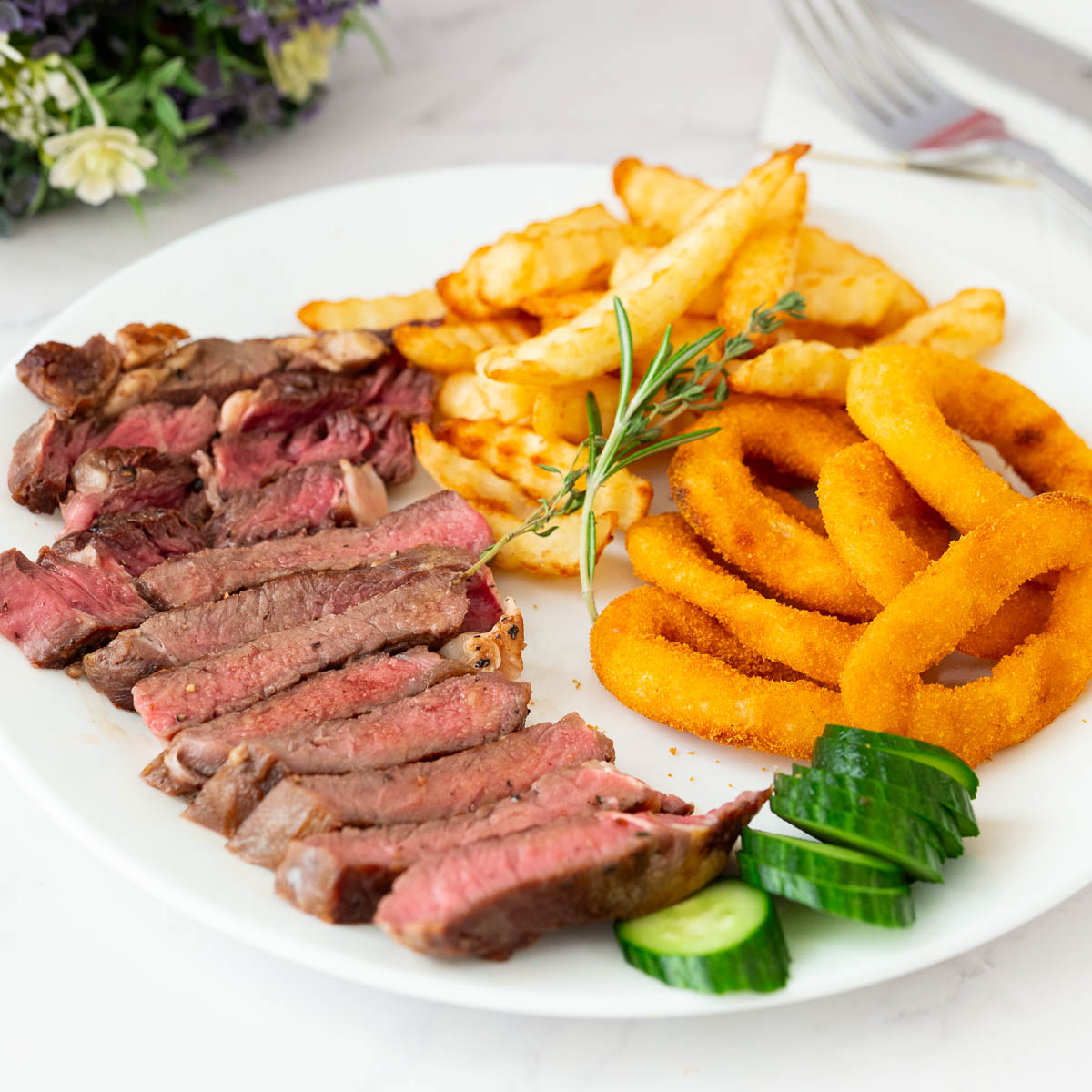 A white plate with pan seared steak on the stovetop.