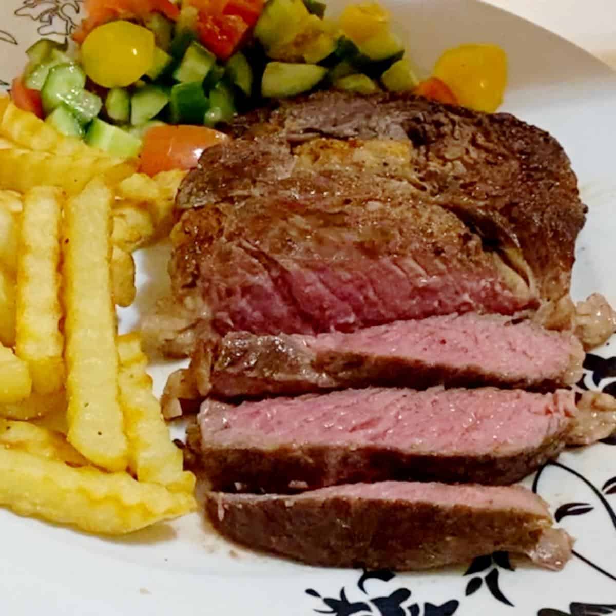 A plate with sliced steak fired and salad.