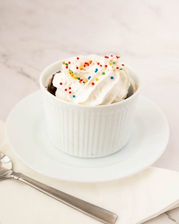 Chocolate mug cake in a ramekin topped with whipped cream.