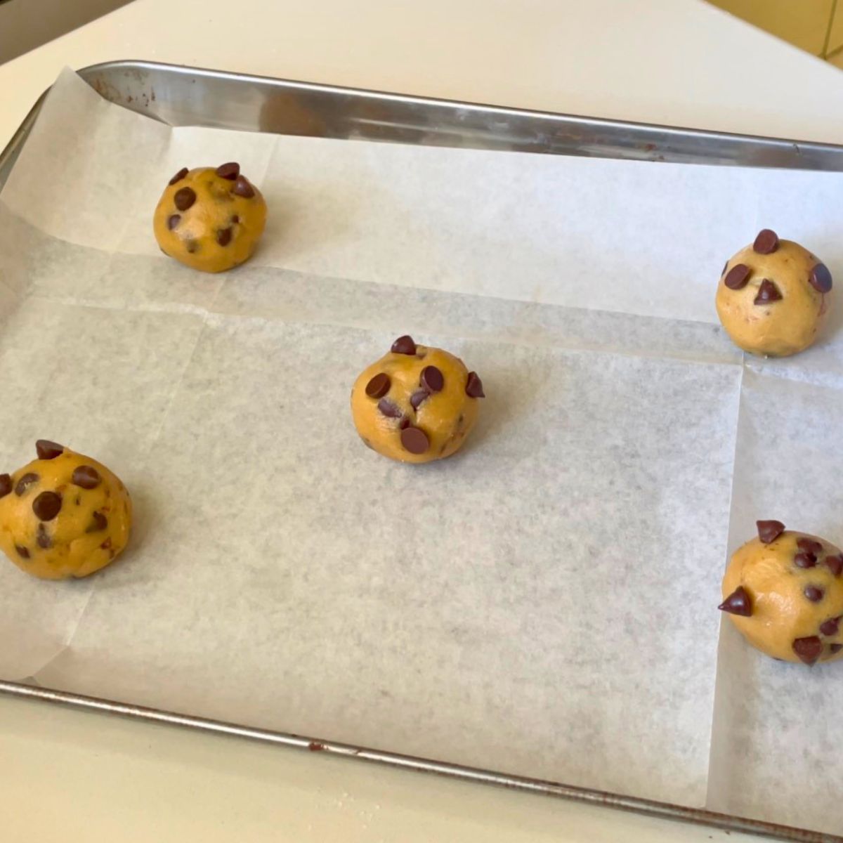 A baking sheet with chocolate chip cookie dough balls.