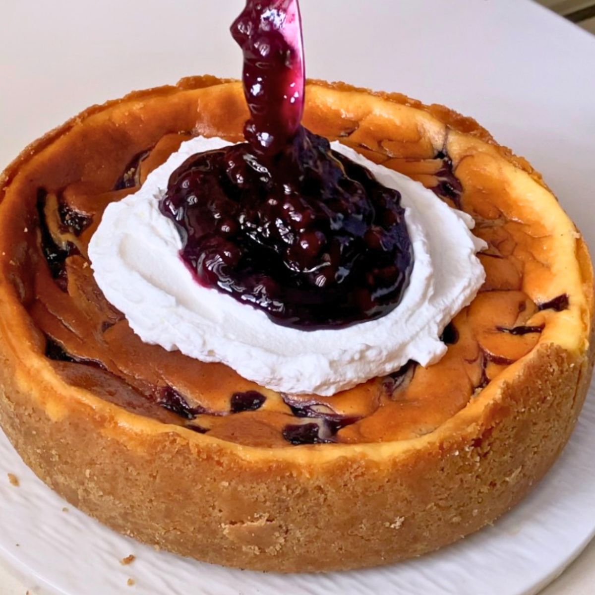 Adding blueberry sauce to the whipped cream on cheesecake.
