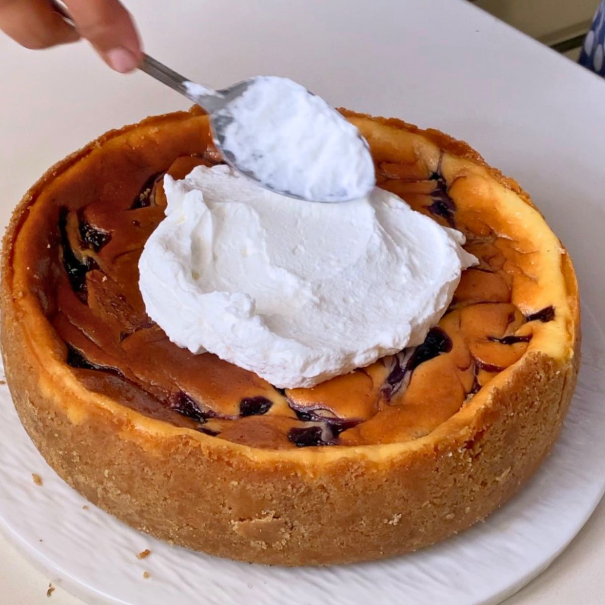 Adding whipped cream to the baked cheesecake.