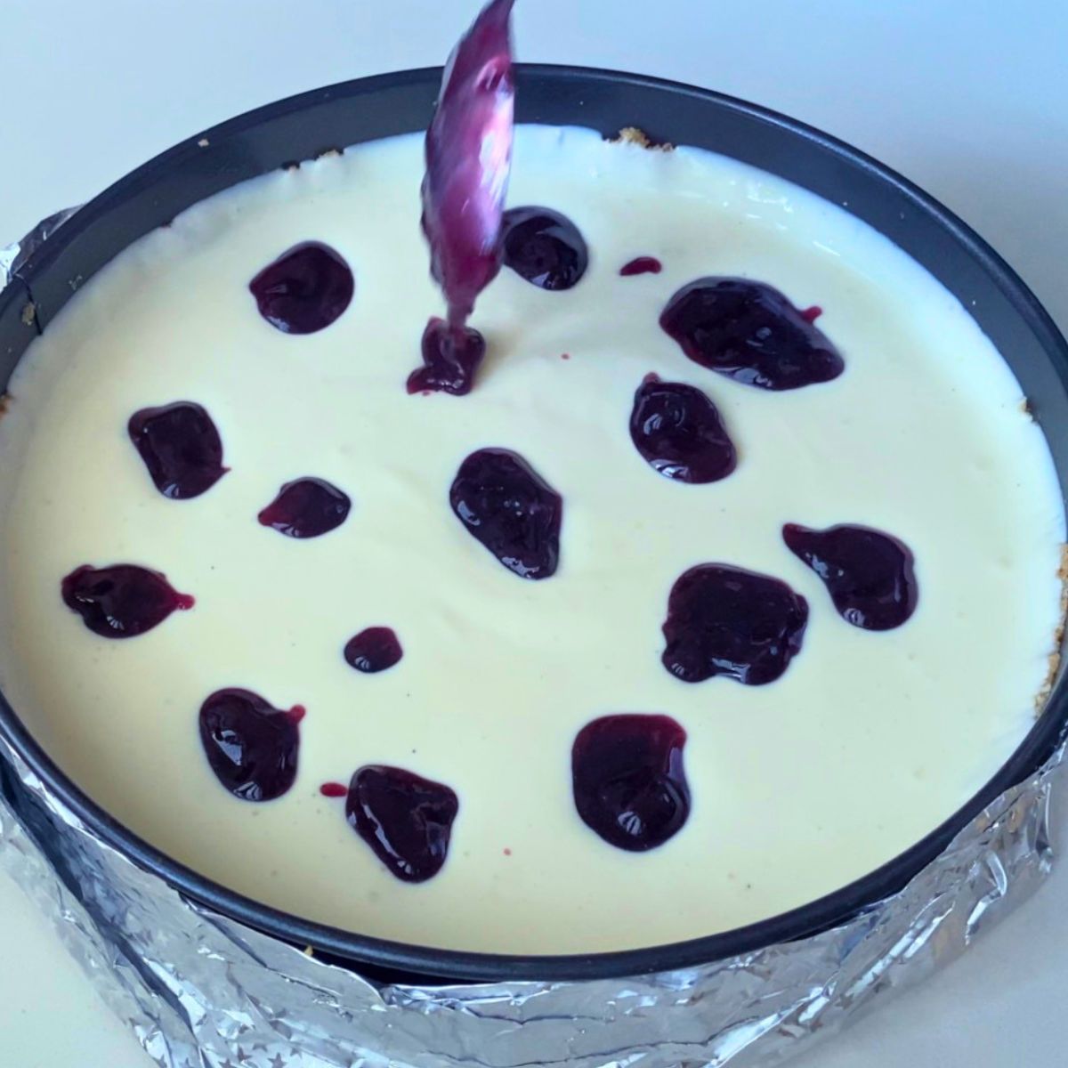 A cheesecake batter with blueberry sauce dollops.