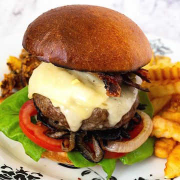 A classic cheese burger on a plate with fries.