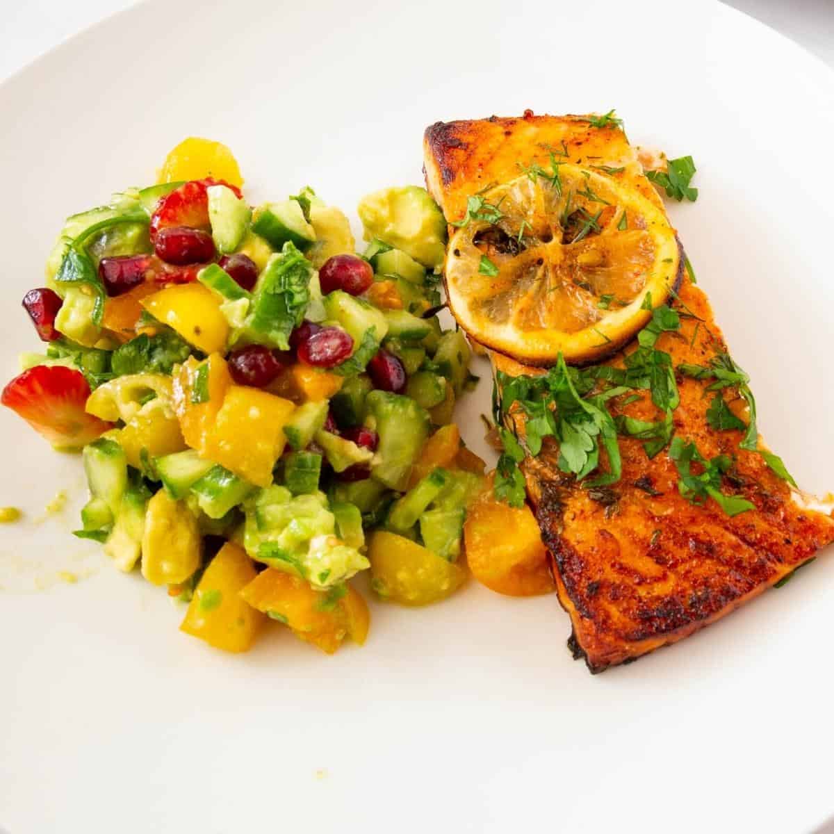 A slice of salmon on a plate with salad.