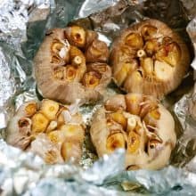 Aluminum foil with four heads of roasted garlic.