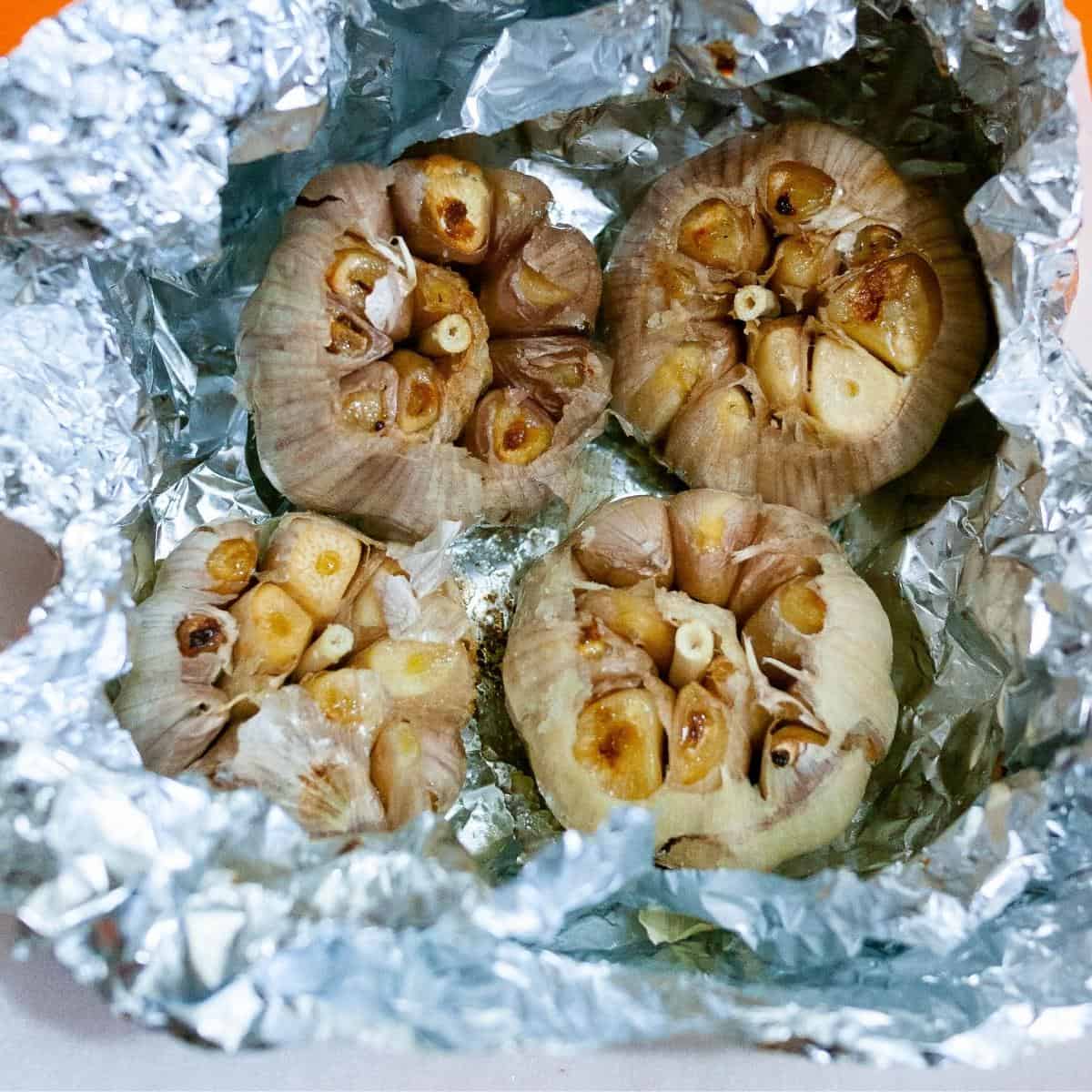 Aluminum foil with garlic heads roasted in the oven.