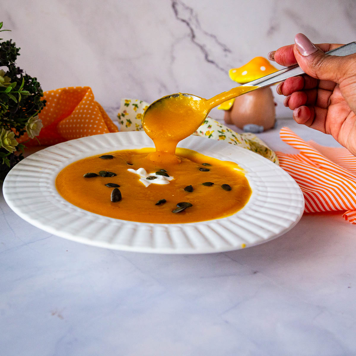 A spoon holding pumpkin soup in a bowl.