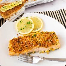 A slice of salmon on a plate topped with breadcrumbs.