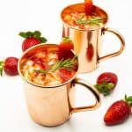 Two copper mugs with moscow mule with strawberies.