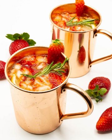 Two copper mugs with moscow mule with strawberies.