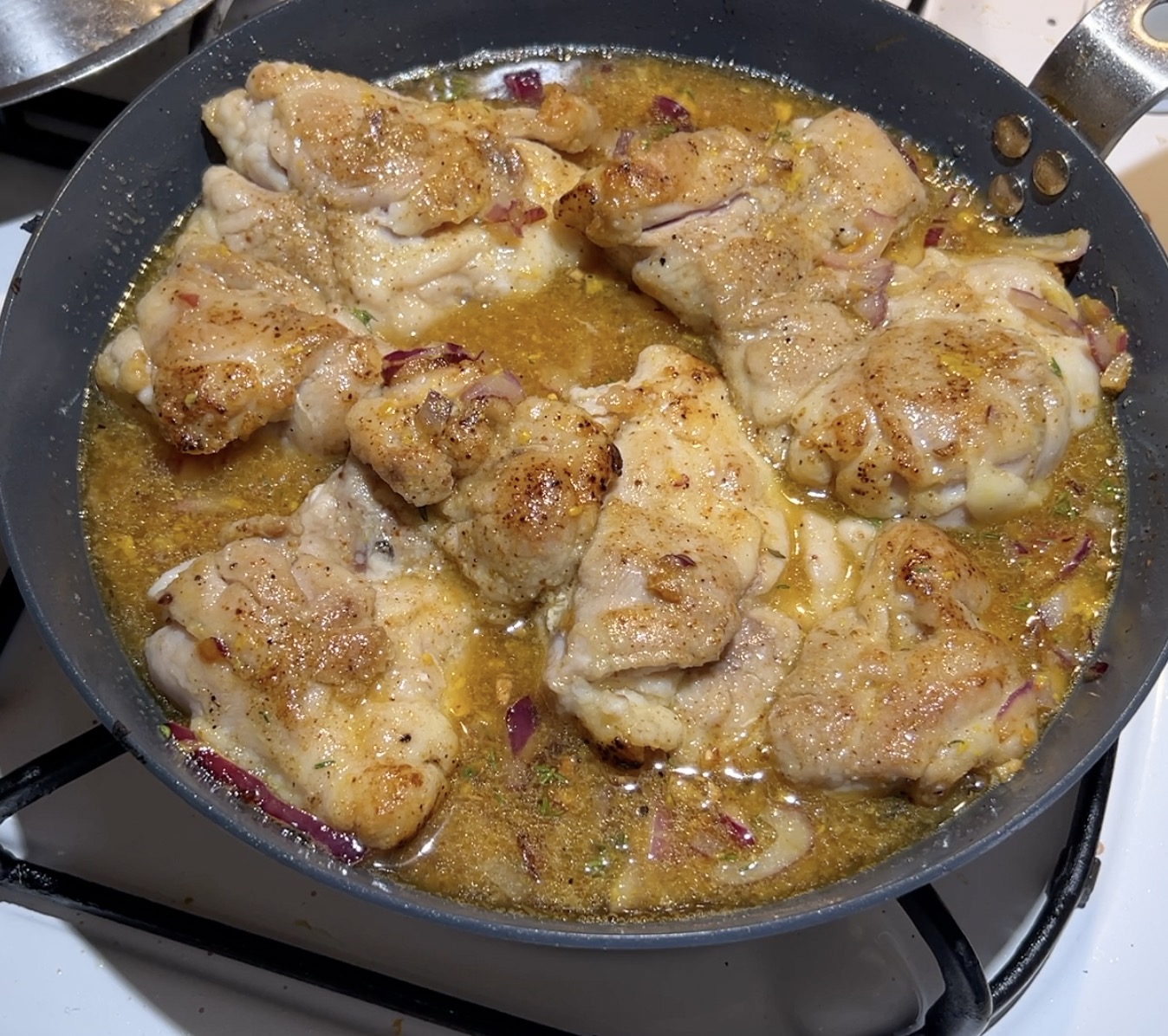 A skillet with chicken simmering in sauce.
