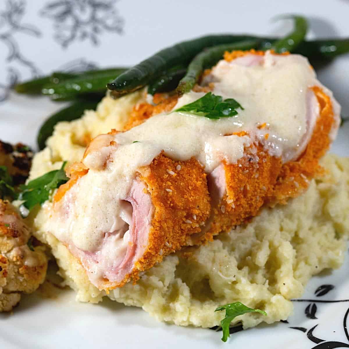 A plate with cordon bleu chicken with cheese sauce.