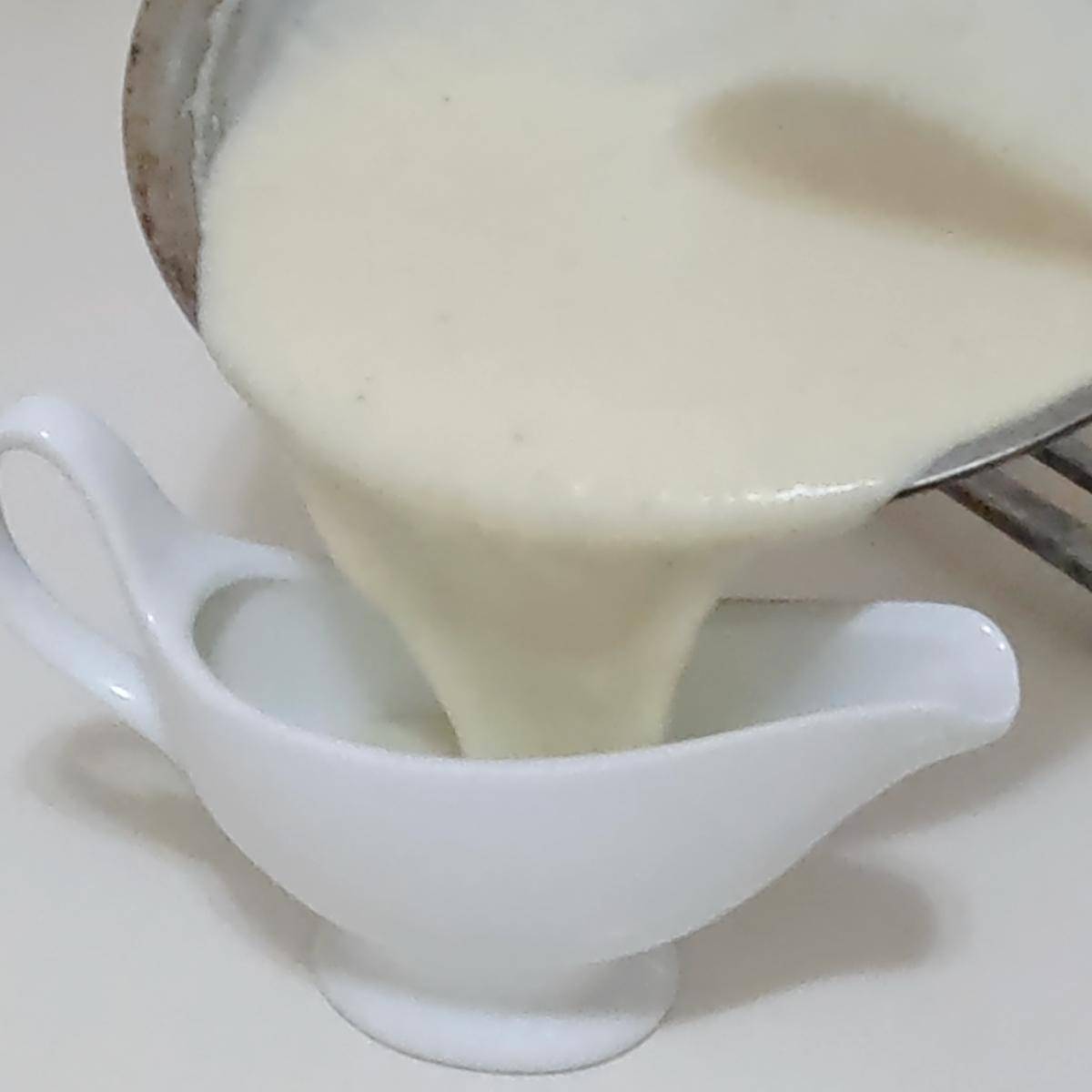 A sauce boat and saucepan with white sauce.