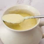A sauce pot with cheese and spoon.