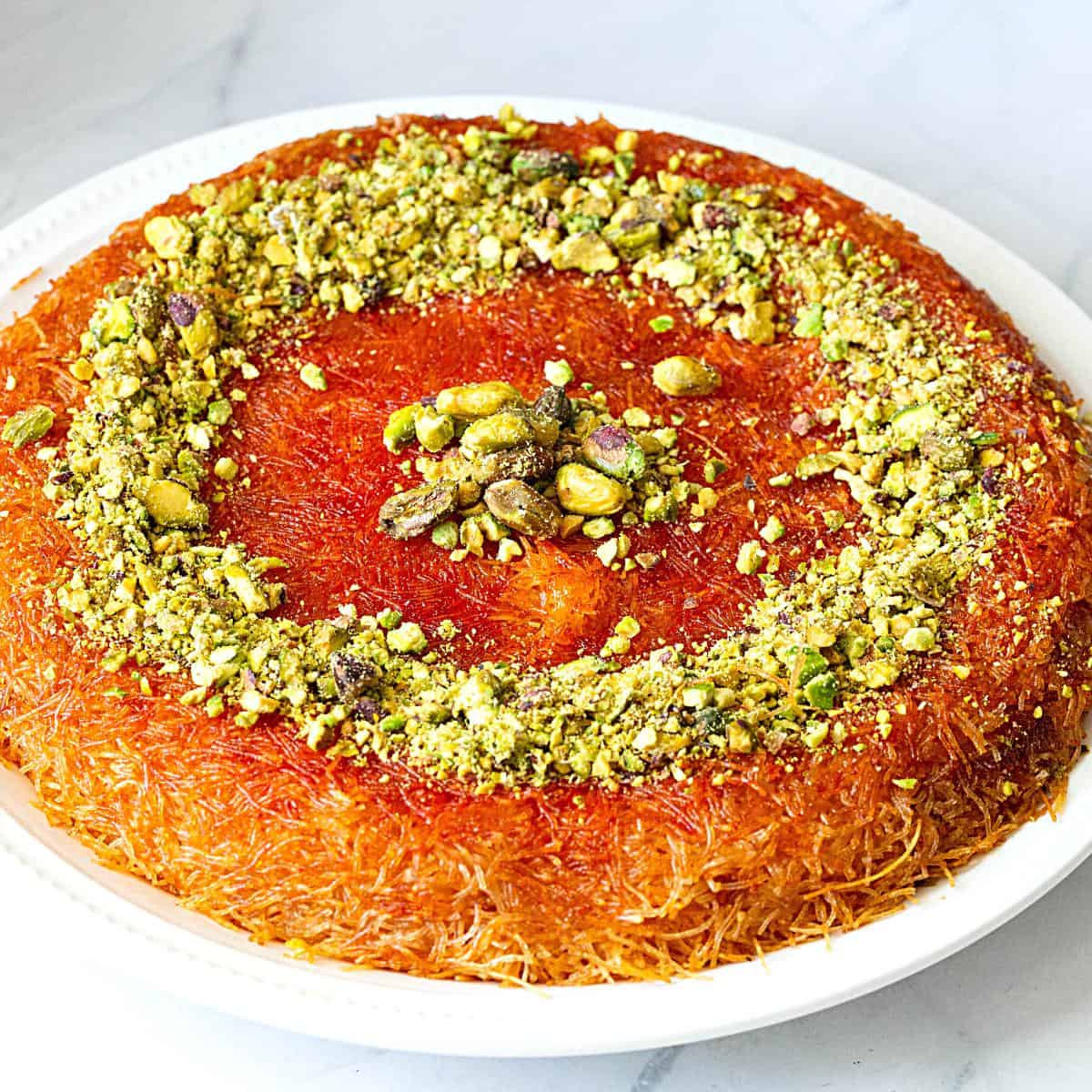 A plate with knafah topped with nuts.