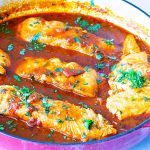 A skillet with salmon and tomato sauce.