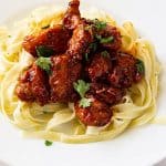 A plate with chicken and noodle in sauce.