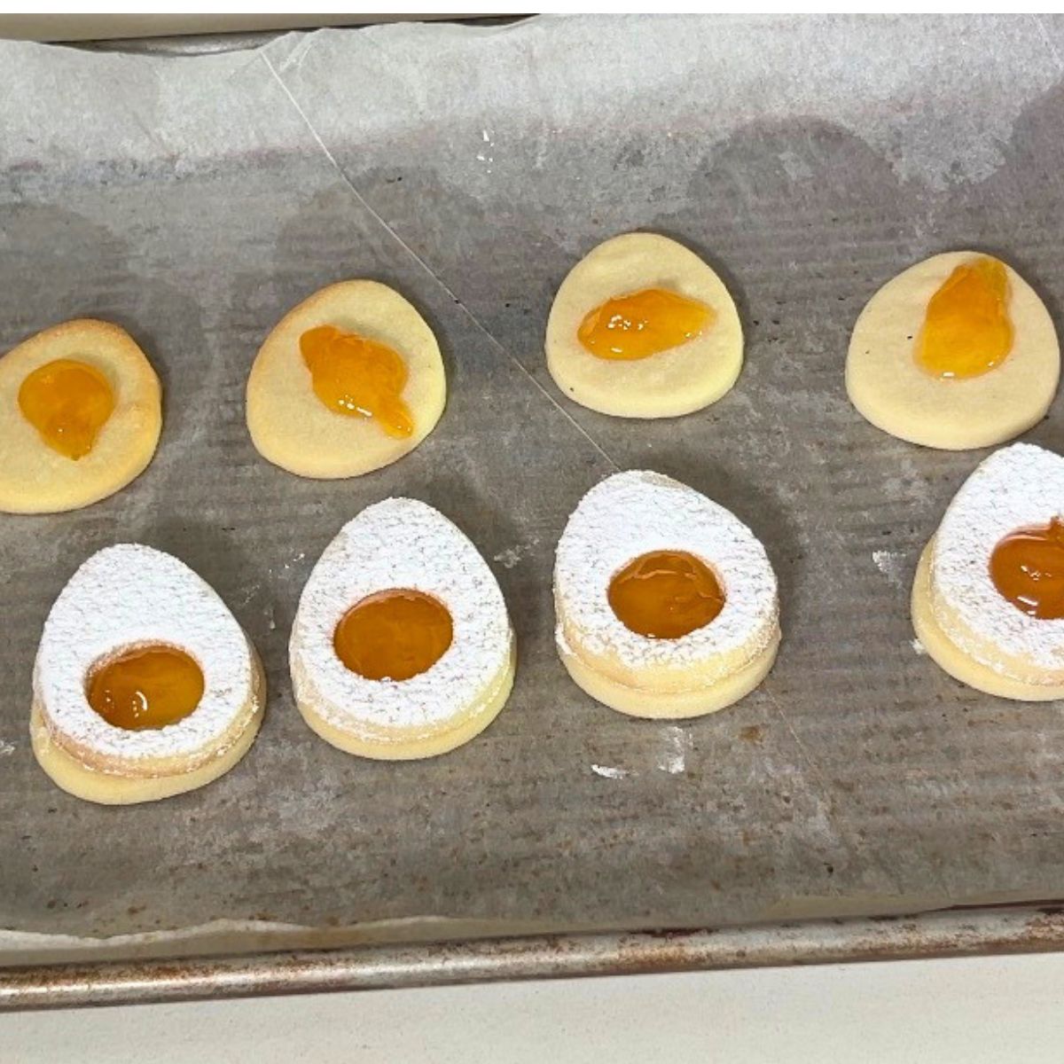 Sandwich sugar cookies with apricot jam on tray.